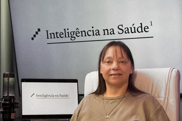 Cassiana Souza Meyer no estúdio do Inteligência na Saúde, com o nome do projeto na parede ao fundo.
